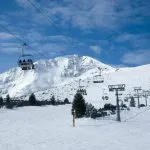 Panoramic wide angle view on white snowy ski slopes , mountain peak and ski chairlift transporting skiers.